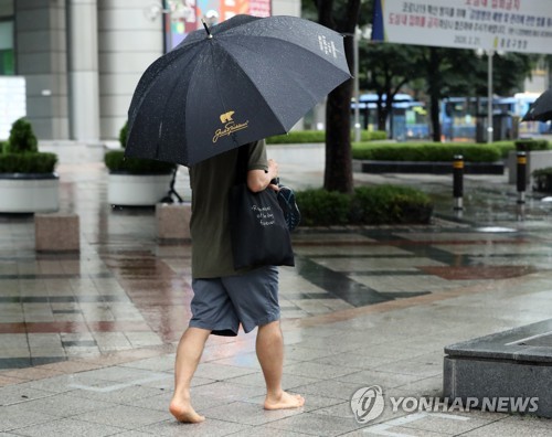 ▲ 1일 정오경 서울 시내에 강한 빗줄기가 쏟아지자 한 시민이 신발을 벗고 맨발로 이동하고 있다.